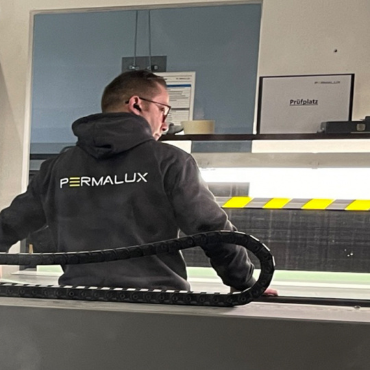 Wasserschneide PERMALUX ein Mitarbeiter am Wasserschneider mit einem Pullover mit PERMALUX-Logo PERMALUX