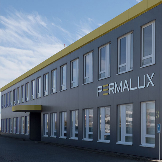 Firmengebäude PERMALUX Graues Firmengebäude von PERMALUX mit Eingangsbereich und Logo PERMALUX